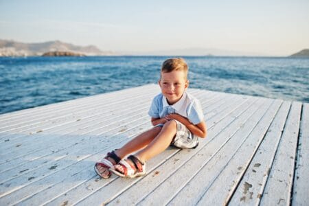 Happy young boy sitting in the floor at the pier against the sea