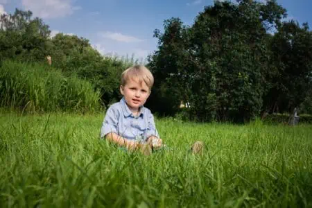 Adorable little blonde boy sitting on the grass at the park