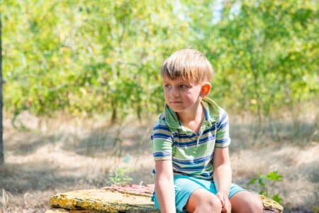 Boy sitting on tree log in the summer park