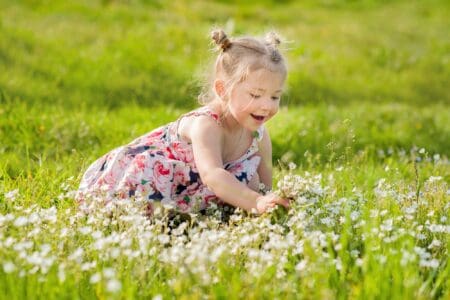 Pretty little girl in summer dress with pigtails sitting in summer meadow