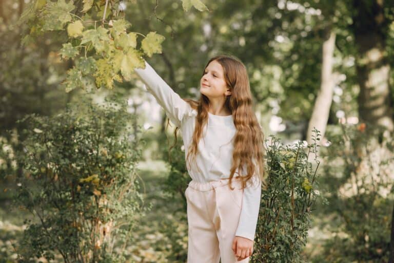 Pretty little girl in white blouse holding tree branch in the park