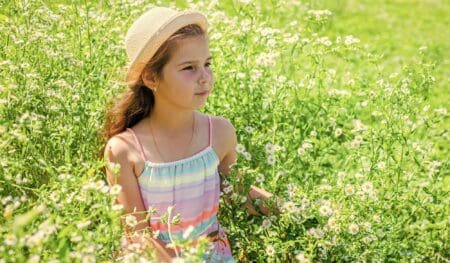 Pretty young girl with summer hat standing on flower field on sunny day