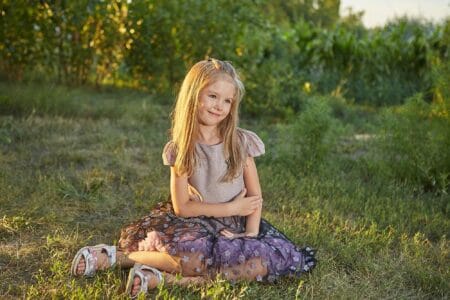 Little charming girl sitting on the grass in the summer garden