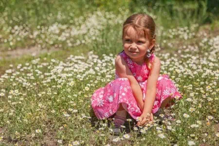 Cute little girl in pink dress sitting in the flowery meadow