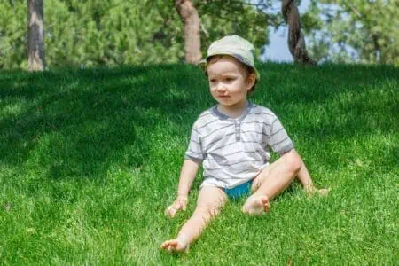 Cute little boy sitting on green grass lawn in the park