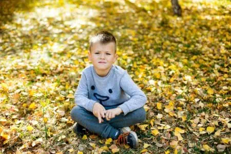 Little boy sitting on the ground covered with autumn leaves