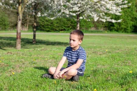 Boy with serious face sitting on the grass in the park on sunny day