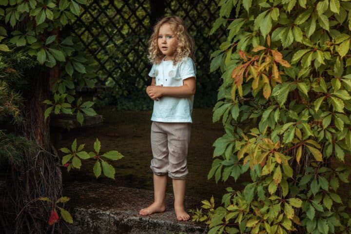 Little blonde curly girl in casual clothes standing barefoot