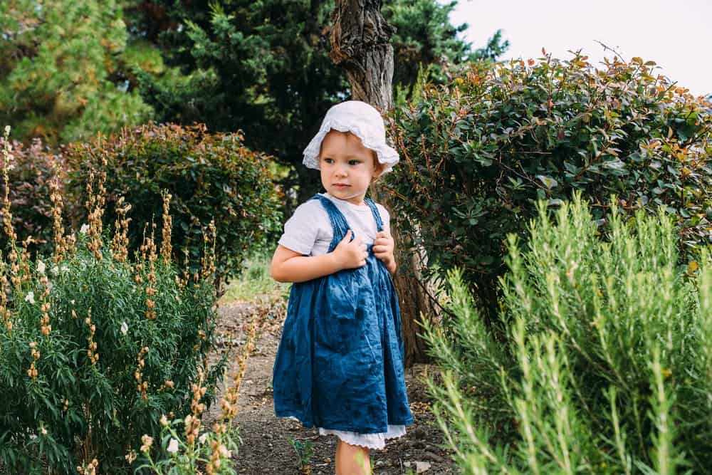 Little girl child standing in the garden among beautiful plants in summer