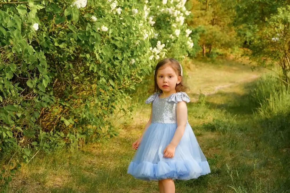 Beautiful little girl wearing blue dress walking in the meadow at the park