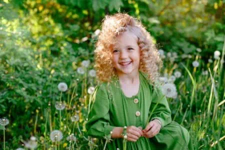 Curly-haired blonde little girl smiling bright in the garden