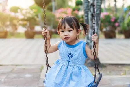 Little girl in blue dress having fun on swing at the park