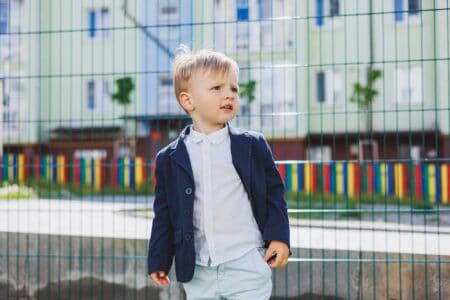 Handsome little boy in shirt and jacket stands on the street