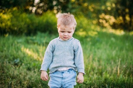 Adorable blonde little boy wearing sweater looking down while standing in the meadow