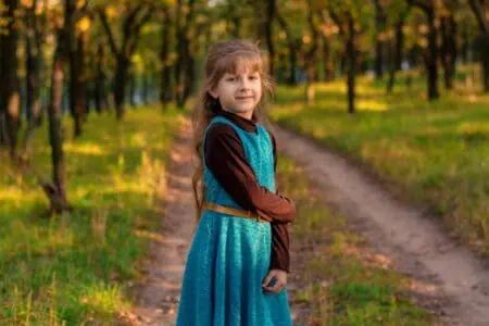 Pretty little girl in blue dress standing in the park during sunset time