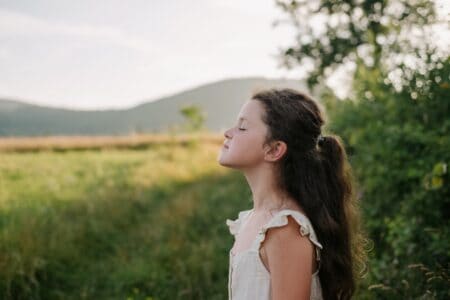 Relaxed little girl with closed eyes in outdoors breathing fresh air from nature during sunrise