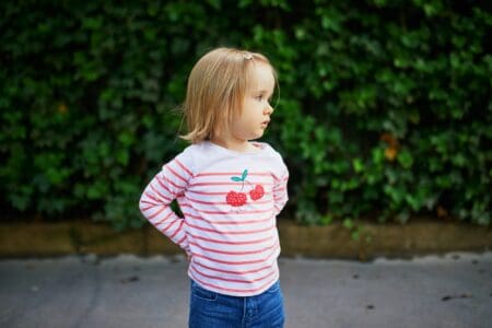 Adorable toddler girl standing behind nature background in the street
