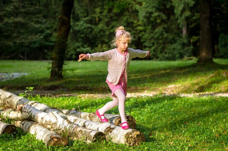 Lovely blond girl balancing in tree trunk in the spring forest