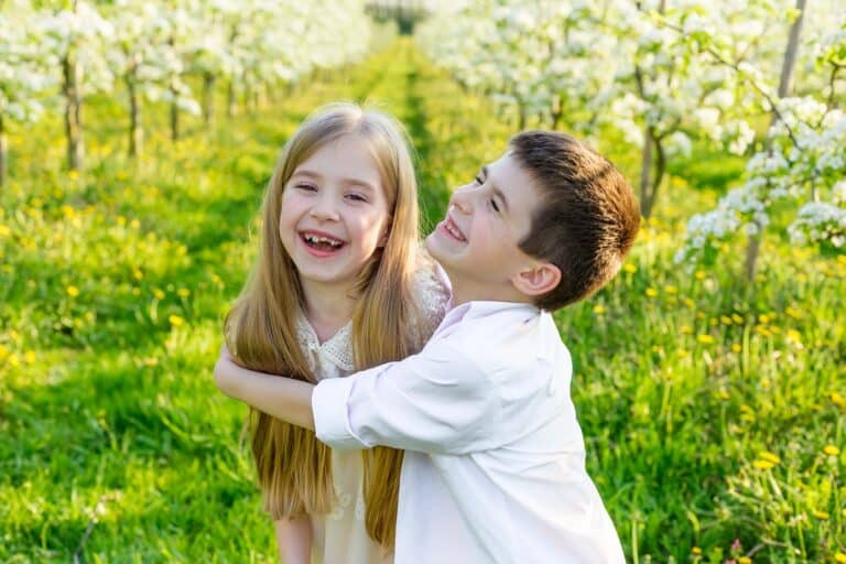 Cheerful young boy hugging his sister and having fun in the flowery garden