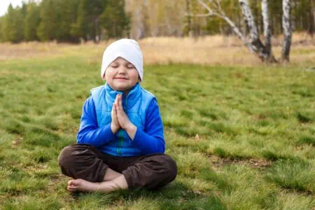 Adorable young boy sits on a green grass while praying