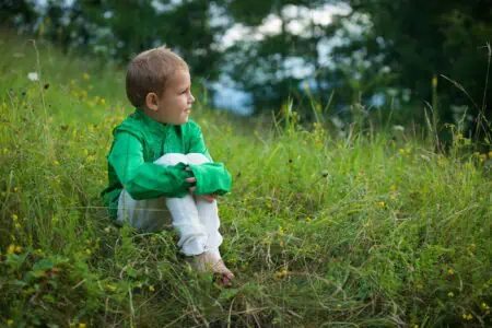 Little boy in green clothing looking sideways while sitting in the meadow