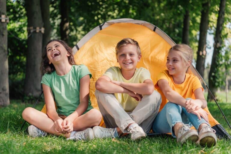 Three kids laughing together sitting on the grass at the park