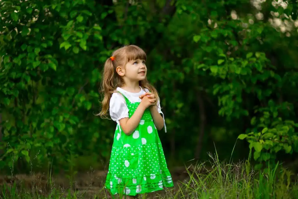 Cute little girl in green floral dress praying outdoors