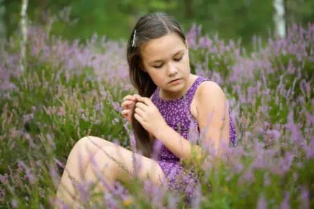 Adorable young girl in purple dress sitting in the middle of heather flowers at the park