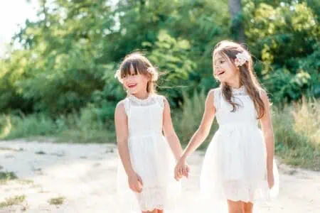Sisters in white dress walking together while holding hands in the forest