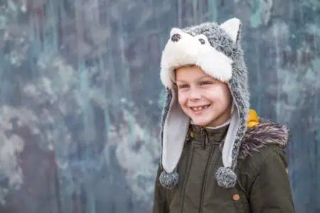Cute young boy in a wolf hat and smiles sweetly on gray background outdoor