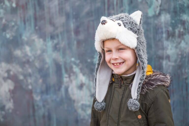 Cute young boy in a wolf hat and smiles sweetly on gray background outdoor