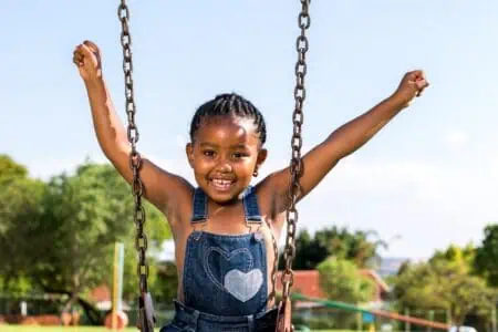 Nigerian little girl raising arms on swing in the park