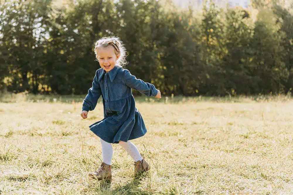 Beautiful little girl with blonde long hair and big blue eyes running in the meadow