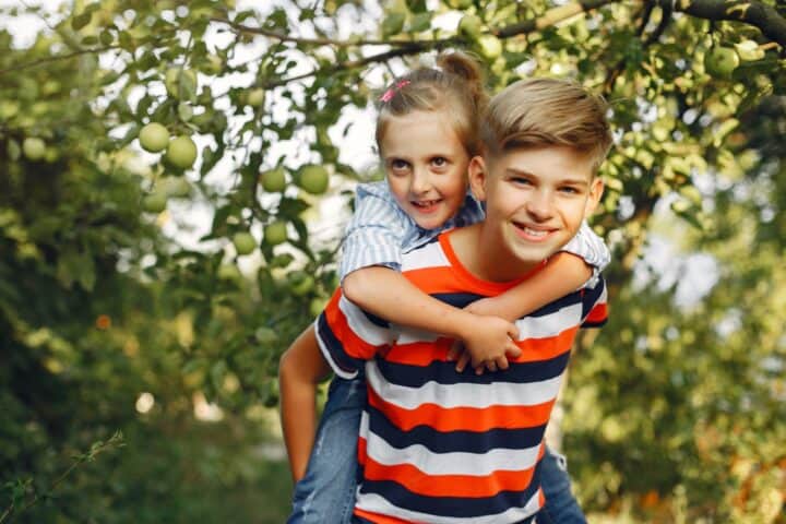 Young boy giving his sister piggyback ride in the park