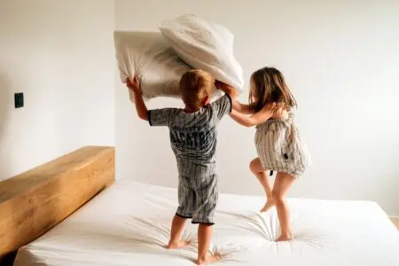 Siblings playing the pillow fight on the bed