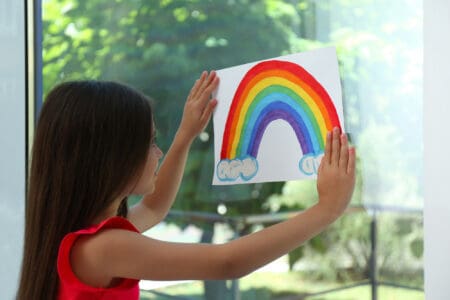 Little girl posting a picture of rainbow on glass windows