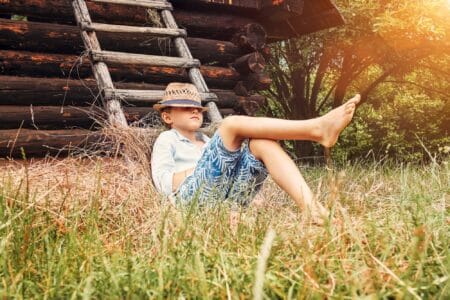 Young boy with cowboy hat lying near old barn in the garden