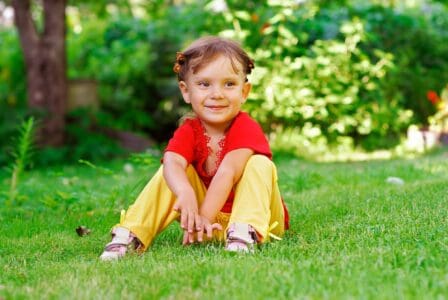 Beautiful little girl sitting on green lawn