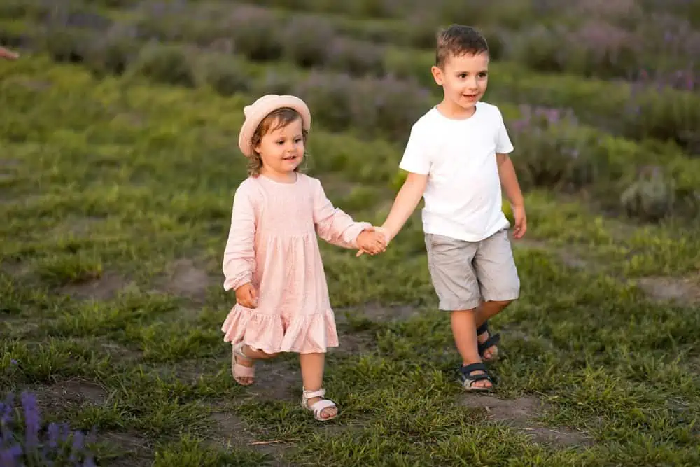Adorable siblings holding hands while walking in the meadow