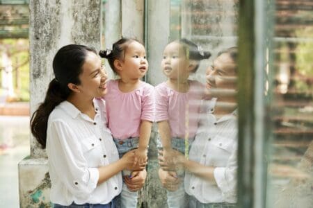 Vietnamese mother and daughter standing at glass window in zoo and looking at animals