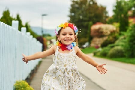 Hawaiian little girl in white dress running down the street with arms wide open