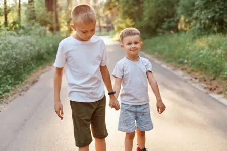 Two adorable young boys in white shirts walking outdoors while holding hands