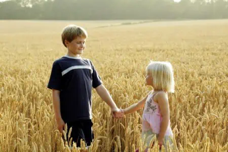 Brother holding sister's hand standing in wheat field