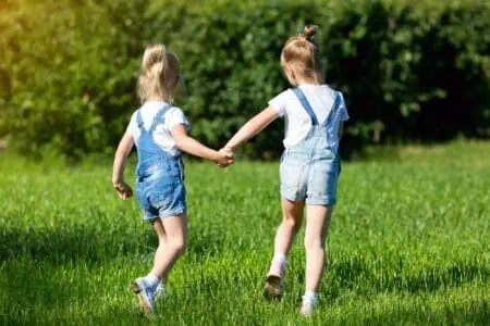 Two girls in denim romper running on the grass while holding hands