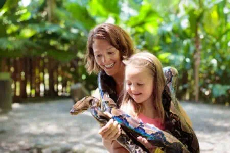 Little girl holding python snake in the zoo with her mother