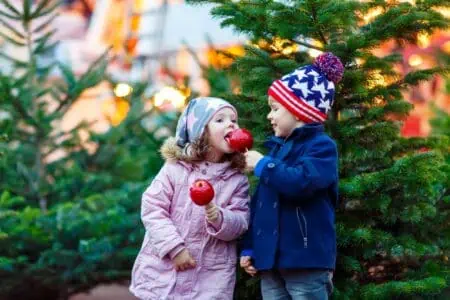 Two little kids wearing winter clothes eating sugar apple in front of trees