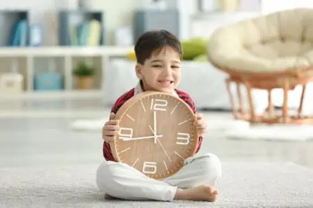 Adorable little boy holding clock sitting on the floor at home