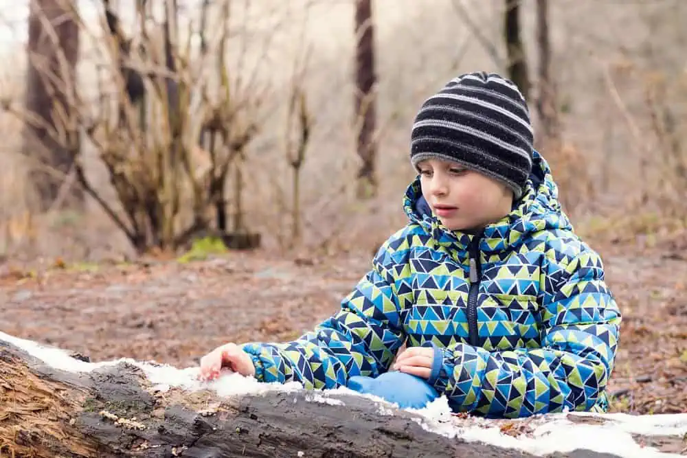 Adorable young boy playing with melting snow in early spring forest