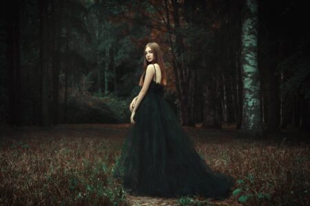 Young girl wearing black dress standing in dark forest environment