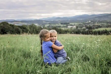Cute girl hugging her brother sitting on the grass